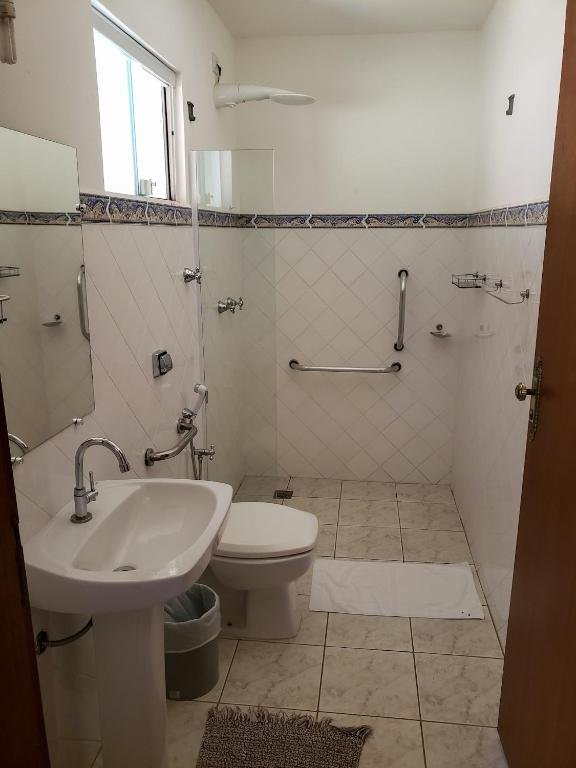 Imagem do banheiro na Pousada Vale dos Dinossauros, para representar o post sobre pousadas em Águas de São Pedro. O ambiente contém barras de apoio perto da privada e chuveiro. A área do box é espaçosa. 