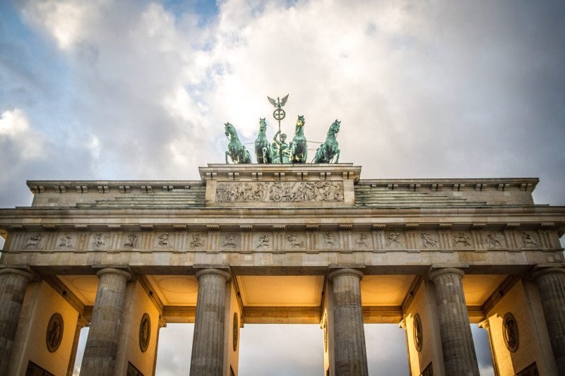 Vista de ângulo baixo do Portão de Brandemburgo, mostrando suas colunas e a escultura da carruagem contra um céu nublado. Esse é um dos destinos indicados no guia de mochilão pela Europa.