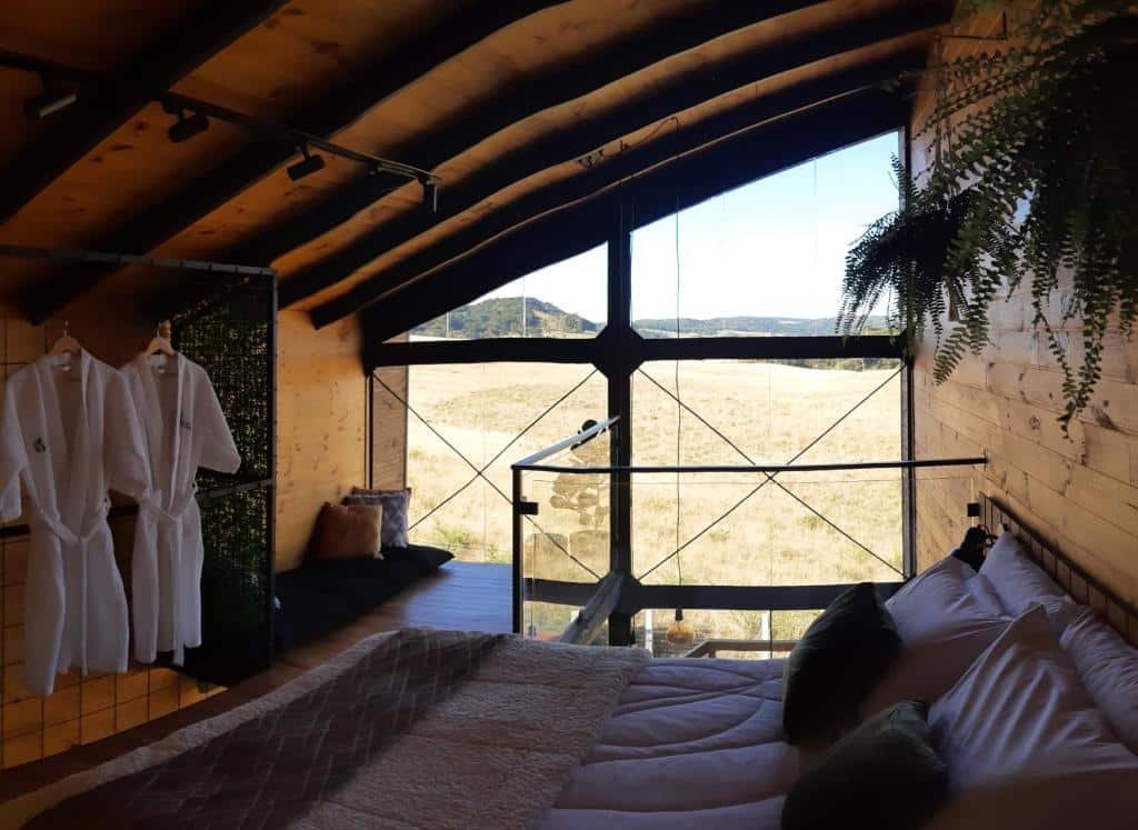 Quarto da Cabana Cambará. Uma cama de casal do lado direito, do lado esquerdo dois roupões.