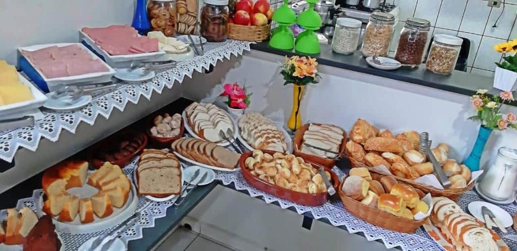 Foto tirada de um buffet de café da manhã na Pousada Portal, em São Pedro. Há muitos pães, frios, frutasa, biscoitos e outros alimentos.