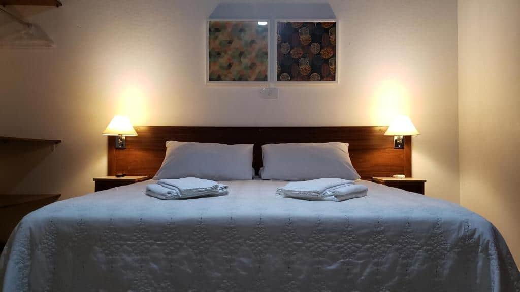 Quarto da Pousada Vale do Dinossauro  com cama de casal, duas luminárias ao lado da cama e um telefone ao lado esquerdo. Ilustra o post de pousadas em Águas de São Pedro.