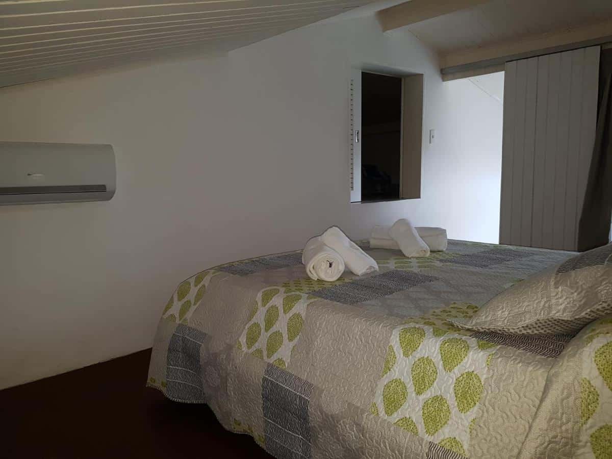 Quarto da Casa- Maresias 3 minutos da praia. Uma cama de casal está  no meio. Na parede em sua frente há um ar-condicionado e uma janela. 