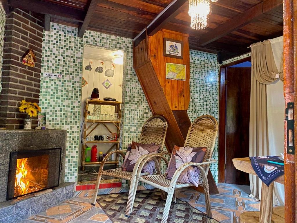 Sala no Chalé Alto na Montanha. Na esquerda há uma lareira, e duas cadeiras com almofadas estão de frente para ela. No fundo há uma porta para a cozinha.