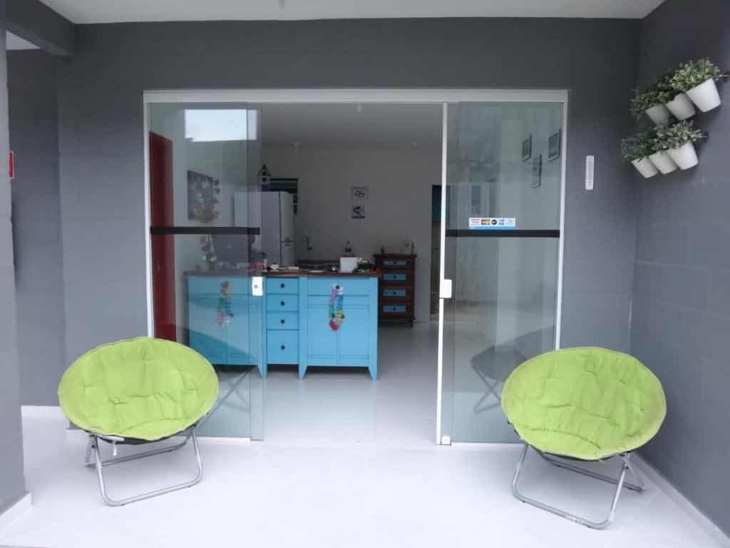 Entrada do Urbano Suites, uma porta de vidro, com uma pequena recepção, alguns vasinhos de flor e duas poltronas em tons de verde claro