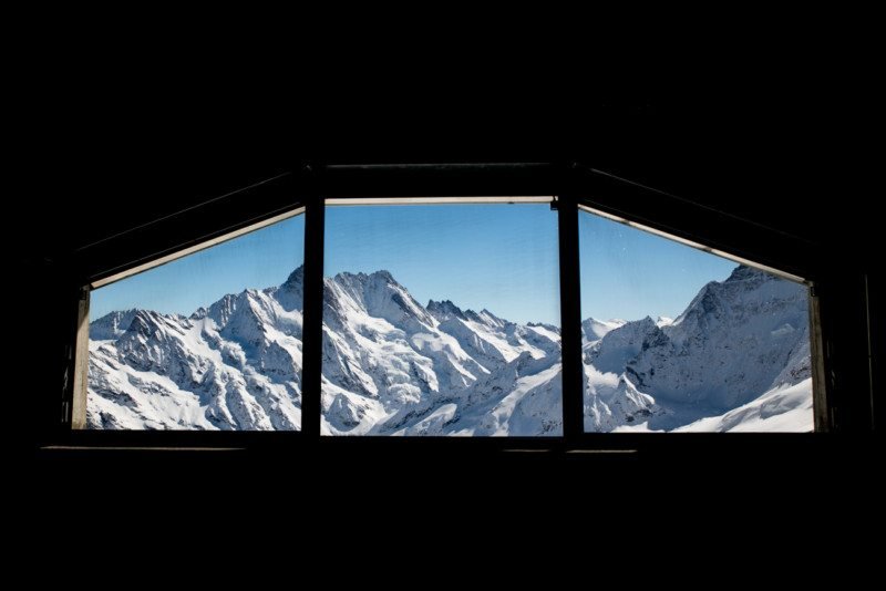 Foto focando a paisagem através da janela da estação de Jungfrau. A vista é para montanhas cobertas de neve.