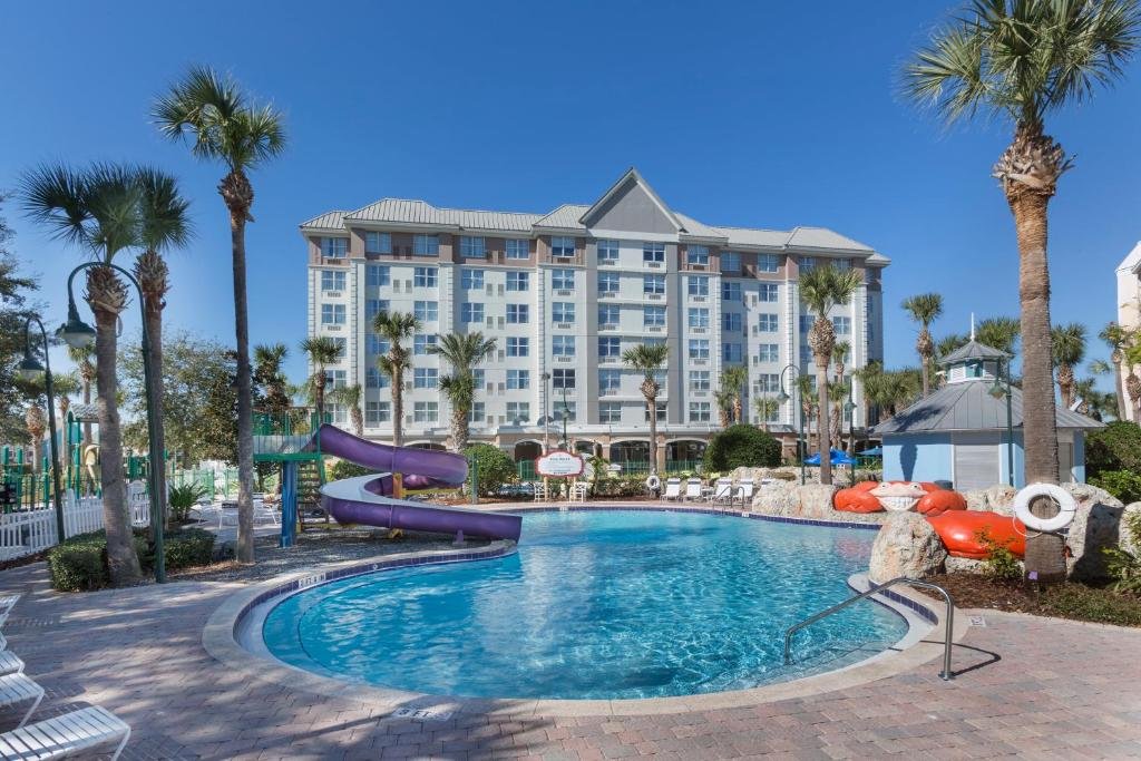 fachada branca que lembra um castelinho com detalhes azuis com uma piscina abaixo com bordas arredondadas e com um tobogã roxo no Holiday Inn Express & Suites S Lake Buena Vista, an IHG Hotel, um dos hotéis em Kissimmee