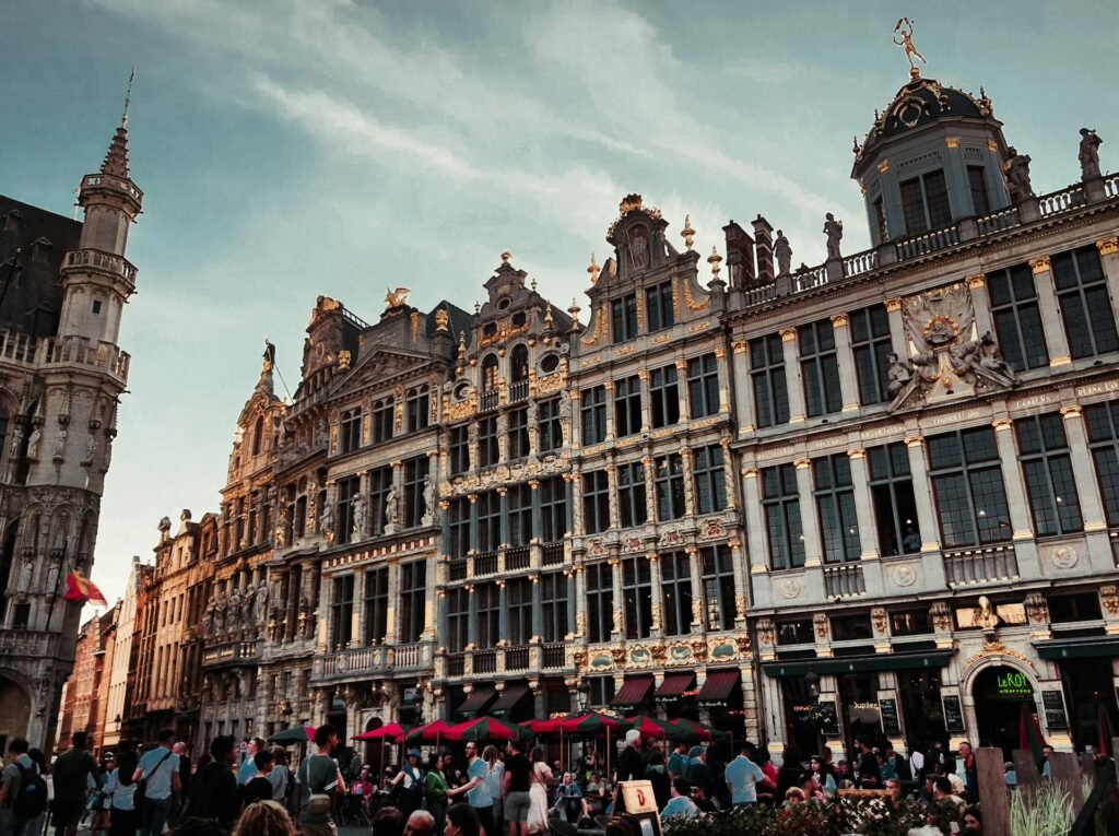 As pessoas se reúnem na Grand, Place, uma praça histórica em Bruxelas cercada por edifícios clássicos e ornamentados sob um céu claro. Esse é um dos destinos indicados no guia de mochilão pela Europa.