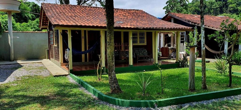 Frente do Chalé super aconchegante em condomínio com garagem durante o dia com jardim a frente e ao fundo a estadia. Representa airbnb em São Sebastião.