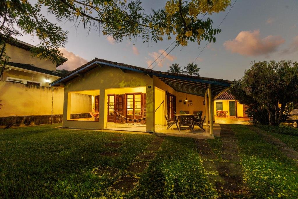 Frente da casa Natureza a 100m da Praia no final do dia com jardim a frente e ao fundo a residência. 