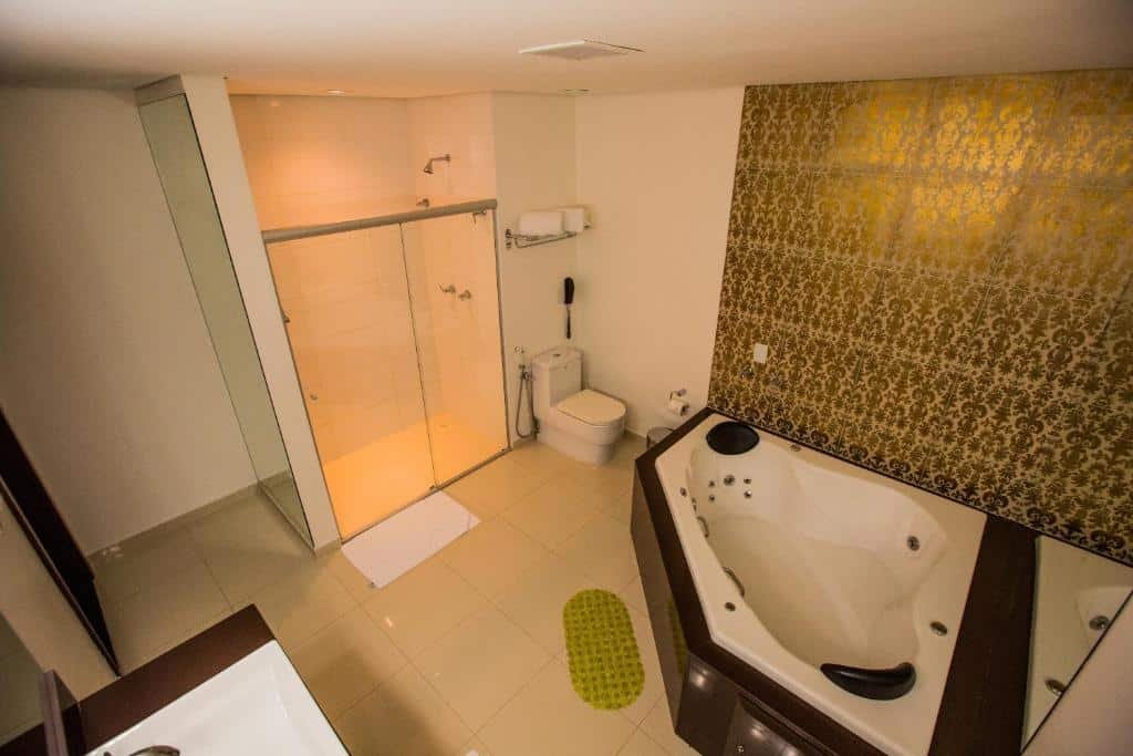 Banheiro do Golden Plaza Hotel. Do lado direito uma banheira de hidromassagem, no meio um vaso sanitário e um box, do lado esquerdo a pia e a porta do banheiro.