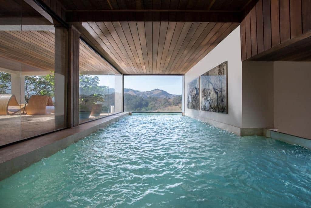 Piscina interna e coberta por um teto de madeira no Botanique Hotel & Spa com uma janela panorâmica dando vista para as montanhas