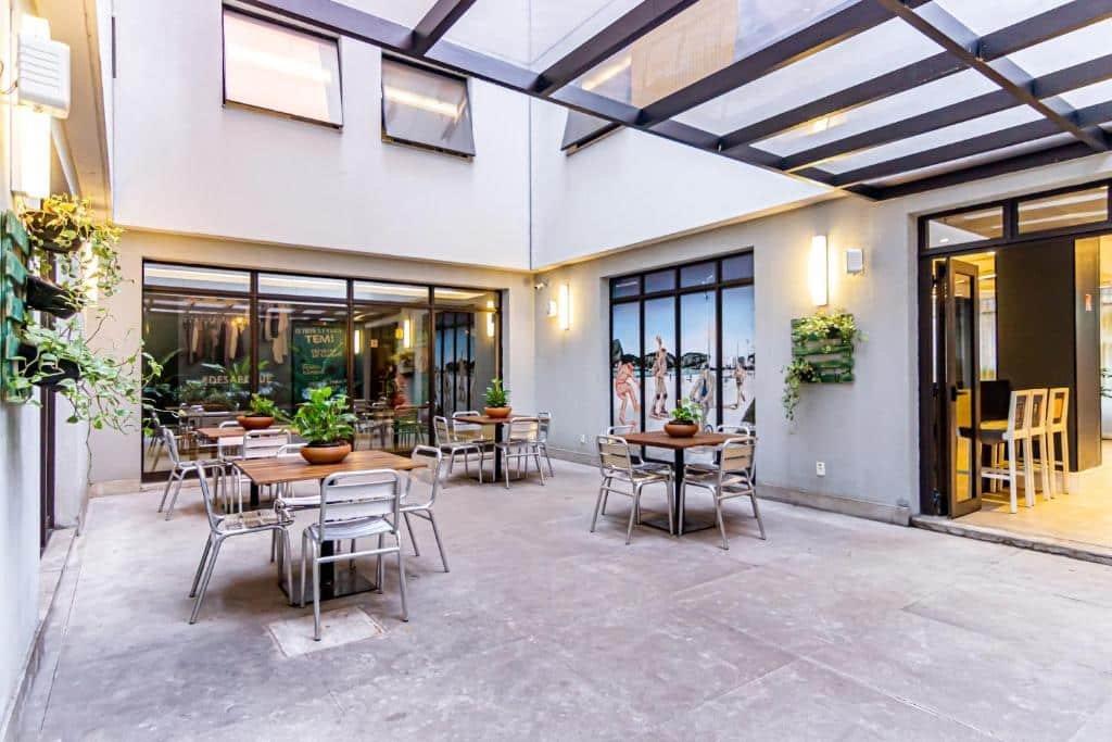 Parte externa do hotel com mesas para quatro pessoas, algumas plantas e uma porta com entrada para a parte de dentro.