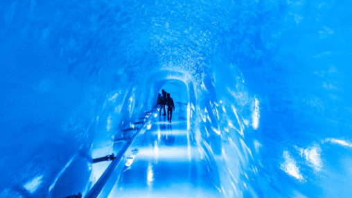 Pessoas caminhando em Jungfraujoch por um túnel de gelo azul brilhante com paredes lisas e um piso brilhante e refletivo. Representa passeios na Suíça.