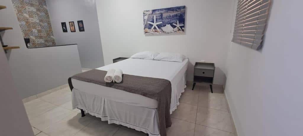 Sala do airbnb KITNET vila do Abraão. No meio do cômodo está a cama de casal, em cada lado da cama há uma pequena cômoda e no lado esquerdo há uma bancada que divide o quarto e a cozinha. Imagem para ilustrar o post airbnb em Ilha Grande.