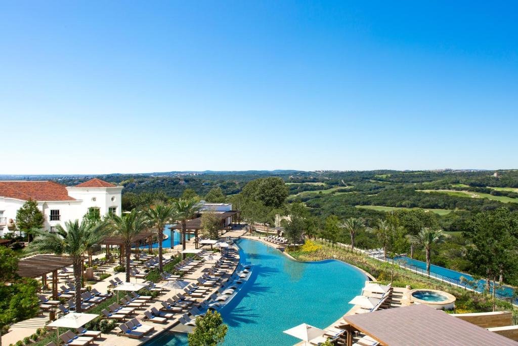 Piscinas do La Cantera Resort & Spa cercado por muito verde, amplos gramados, árvores e pequenas montanhas, nas laterais das piscinas há espreguiçadeiras