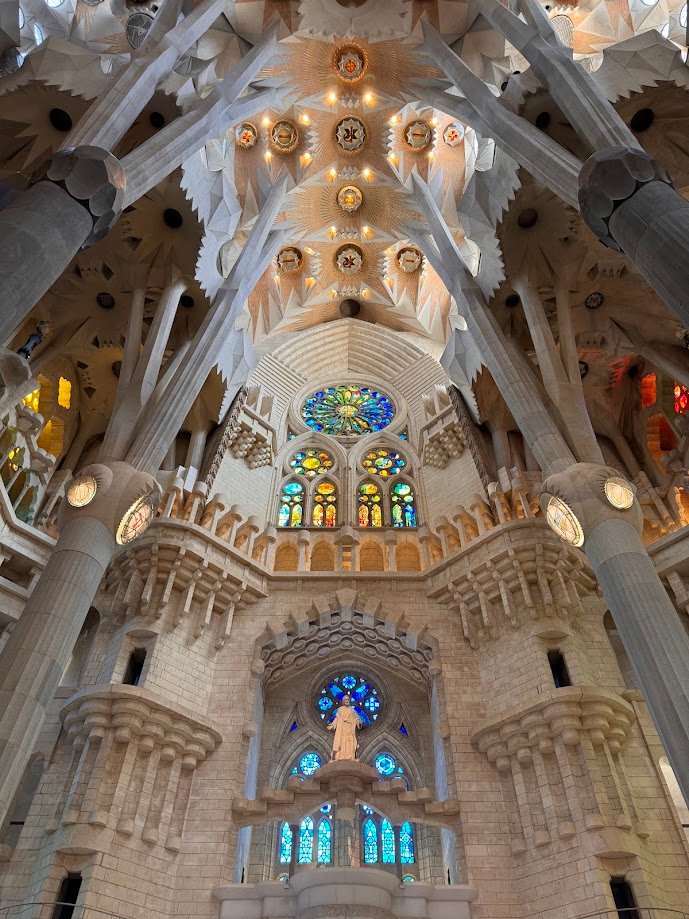 Vista interna da Igreja da Sagrada Família de Barcelona com desenhos intrincados de teto e vitrais coloridos. Colunas se erguem em direção ao teto arqueado. Esse é um dos destinos indicados no guia de mochilão pela Europa.