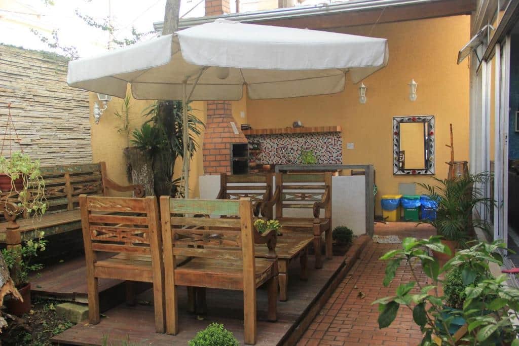 Área de lazer da Pousada dos Franceses. Um guarda-sol no canto esquerdo e quatro cadeiras de madeiras. Atrás uma área com churrasqueira.