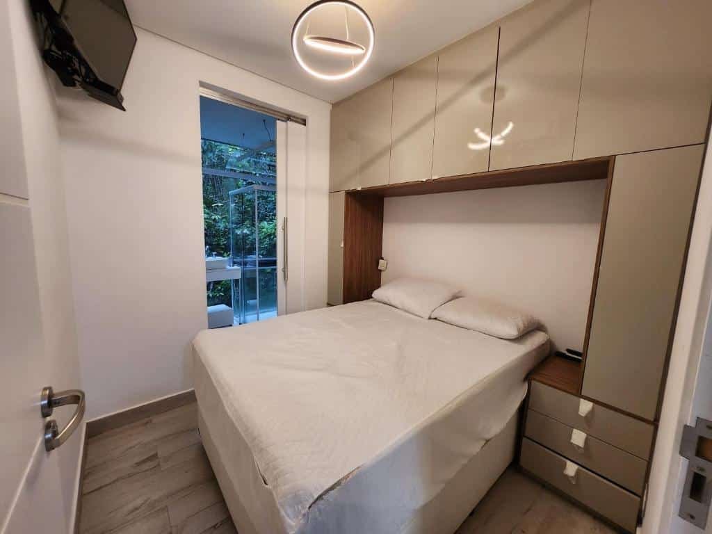 Quarto do Maresias Beach Home - Mata Azul. Uma cama de casal está encostada na parede, no meio de um armário embutido. Ao seu lado está a porta para o banheiro. No alto da parede oposta a cama está pendurada a tv. Este também é um dos airbnb em Maresias.