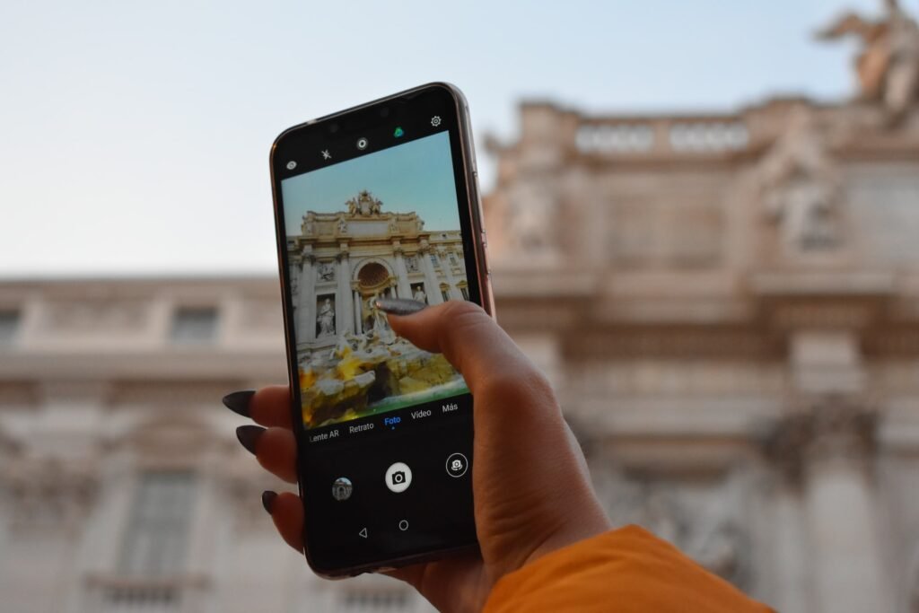 Uma mão feminina com unhas longas segurando um celular na direção da Fonte di Trevi em Roma