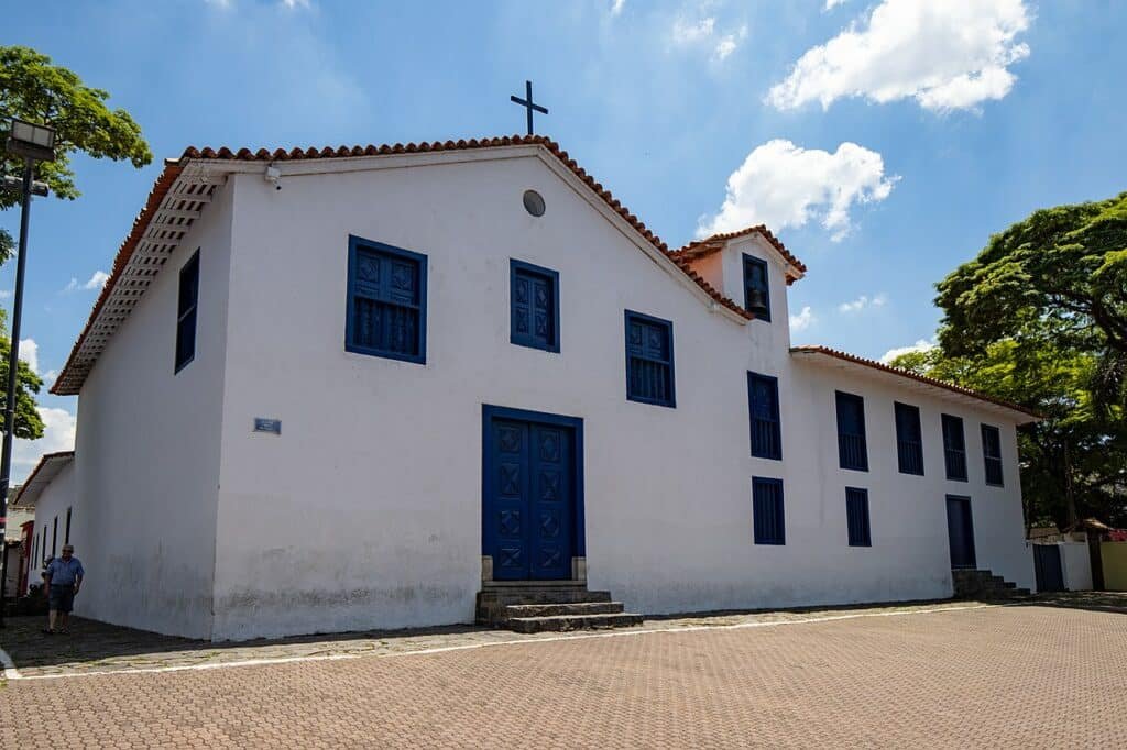 Uma Igreja branca, com janelas no tom azul escuro. Uma porta na frente com uma pequena escada. 
