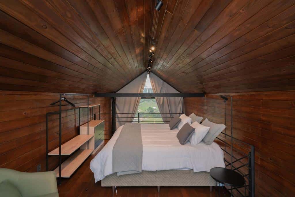 Quarto do Nordic Cabanas. Uma cama de casal do lado direito, do lado esquerdo estantes e uma poltrona.