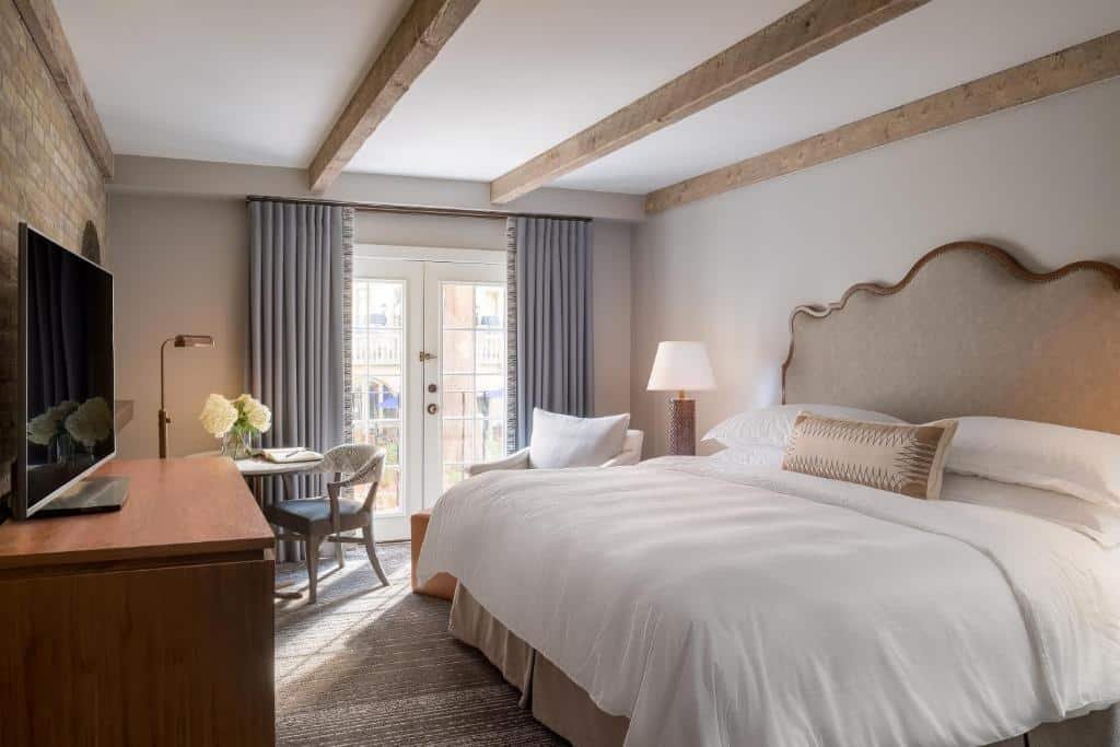 Quarto do Omni La Mansion del Rio com uma varanda com portas de vidro, uma cama de casal, uma poltrona e uma mesa pequena redonda com uma cadeira, há também uma televisão e um abajur de chão no ambiente