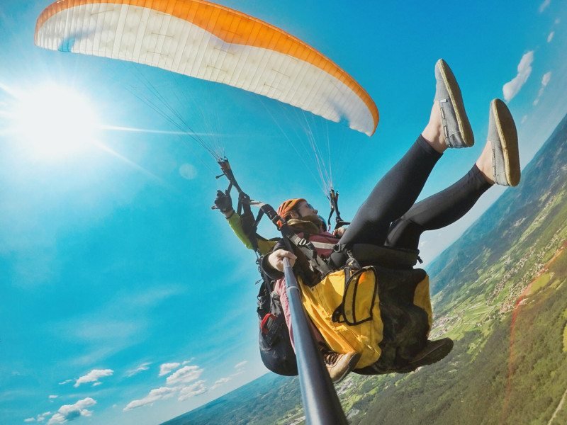 voo de parapente em buzet com uma mulher segurando um pau de selfie ao se fotografar nos ares. O céu está azul e uma parte do solo verde é possível de ser visto da imagem.