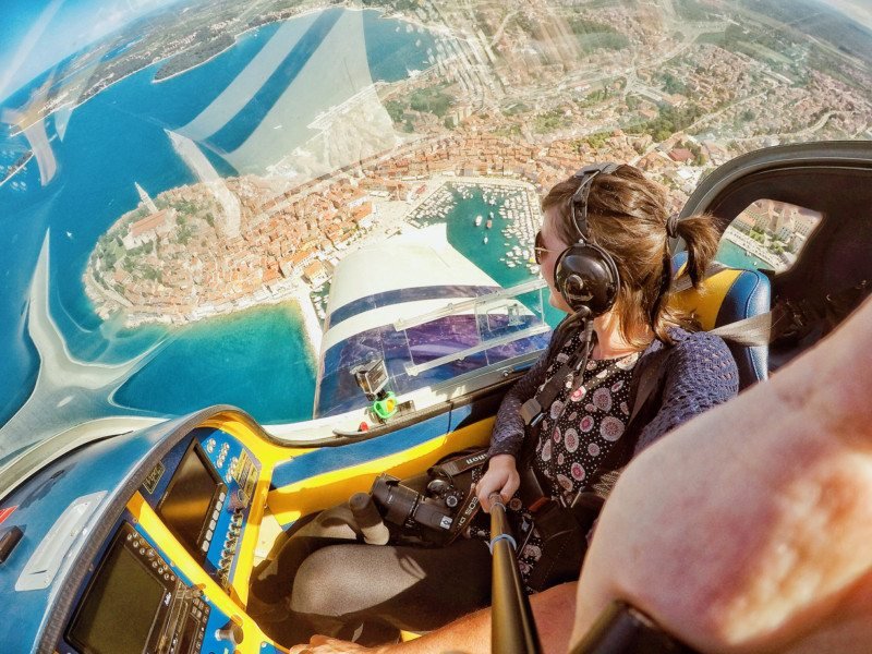 mulher tirando foto de si mesma dentro de um avião sobrevoando a cidade de Vrsar, é possível ver boa parte da cidade há muito metros de distância
