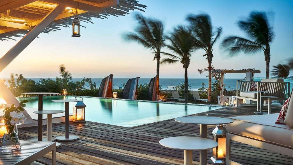 Piscina do The Chili Beach Private Resort com mesas em volta.