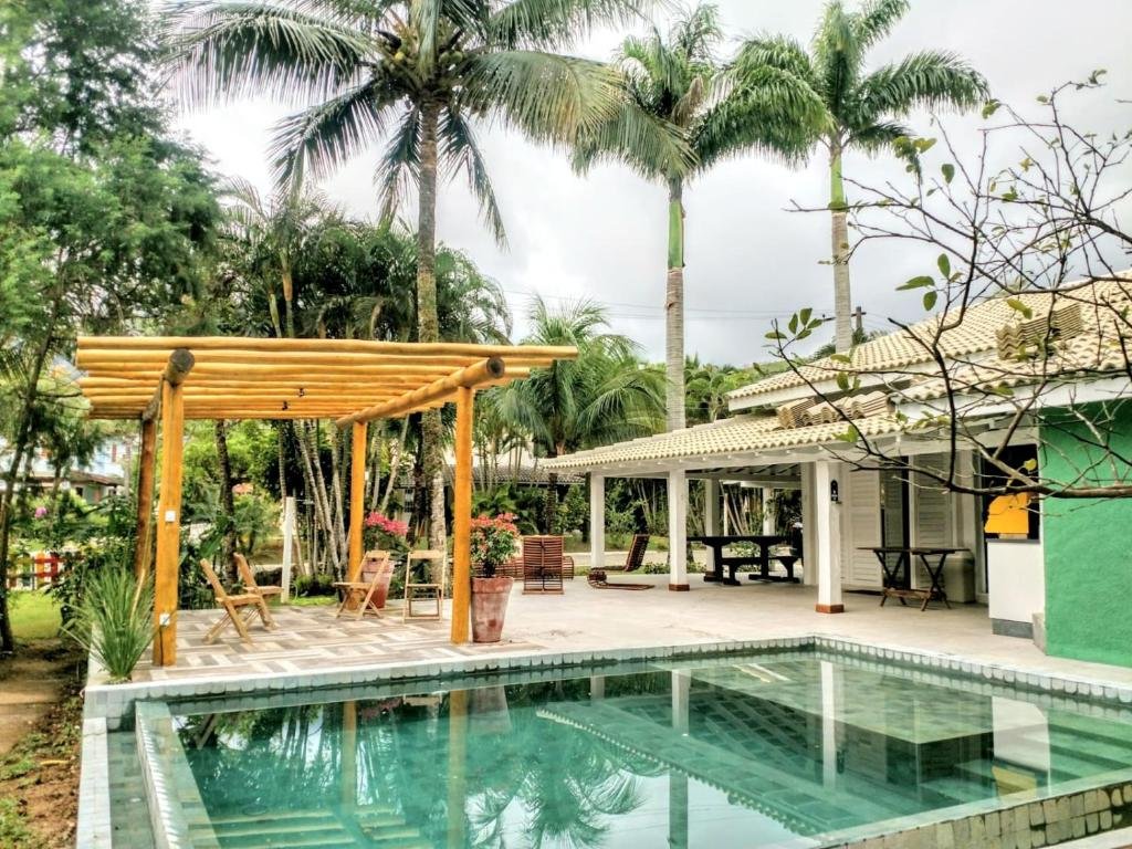 Área de lazer da Linda Casa Praia de Pauba em condomínio durante o dia com piscina a frente e do lado direito ao fundo a estadia.