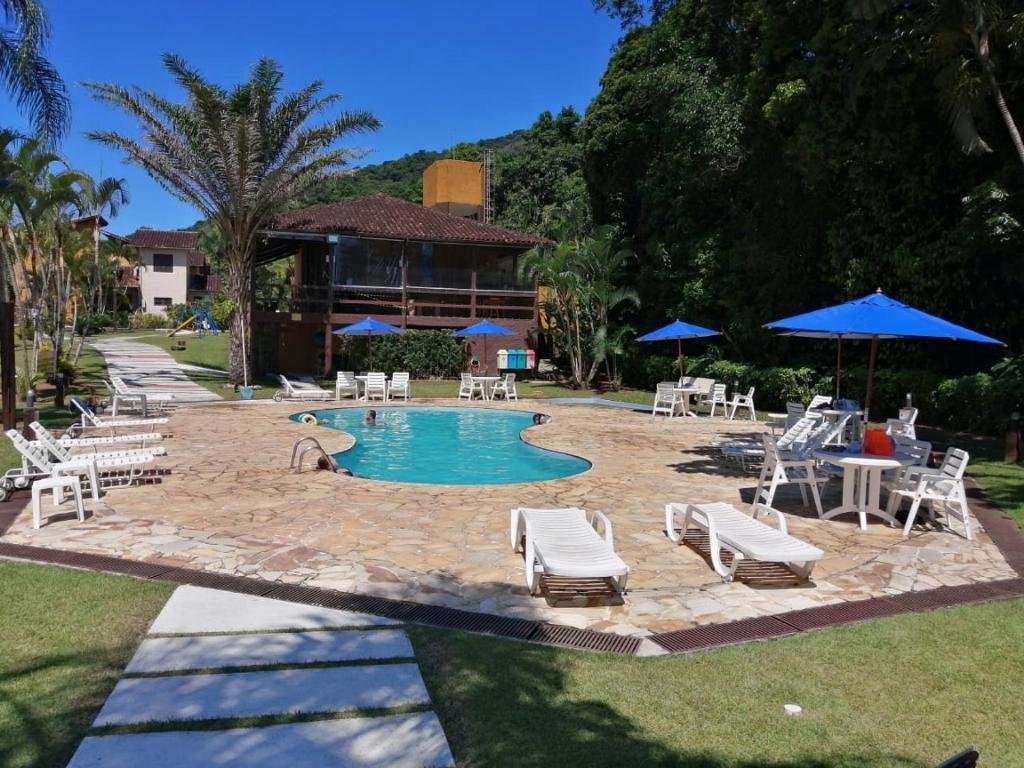 Vista da área de lazer do indo chalé em Boiçucanga Condomínio durante o dia com piscina ao centro e em volta cadeiras e ao fundo a estadia.