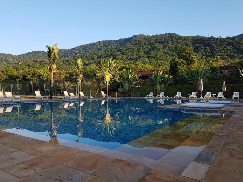 Piscina ao ar livre do Maresias Beach Housing durante o dia com piscina a frente e ao fundo várias cadeiras.