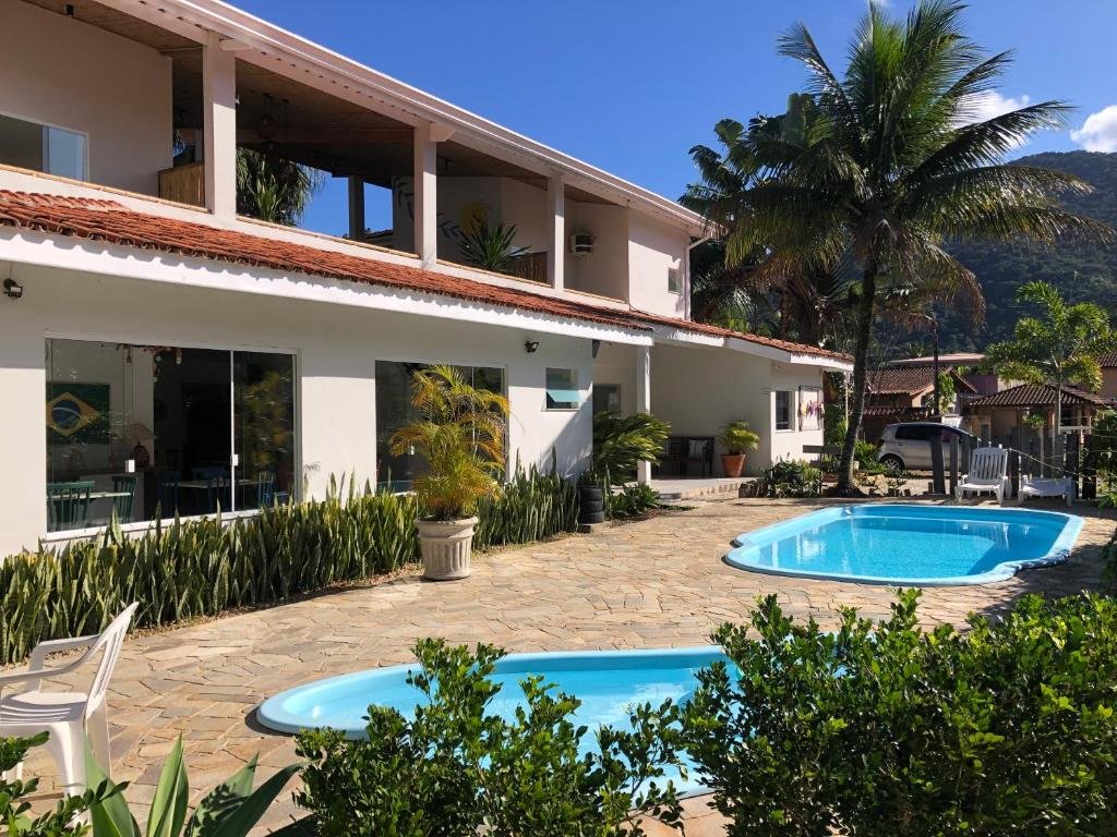Área externa da Pousada Baía das Conchas. Duas piscinas no meio, na frente árvores, do lado esquerdo a propriedade.