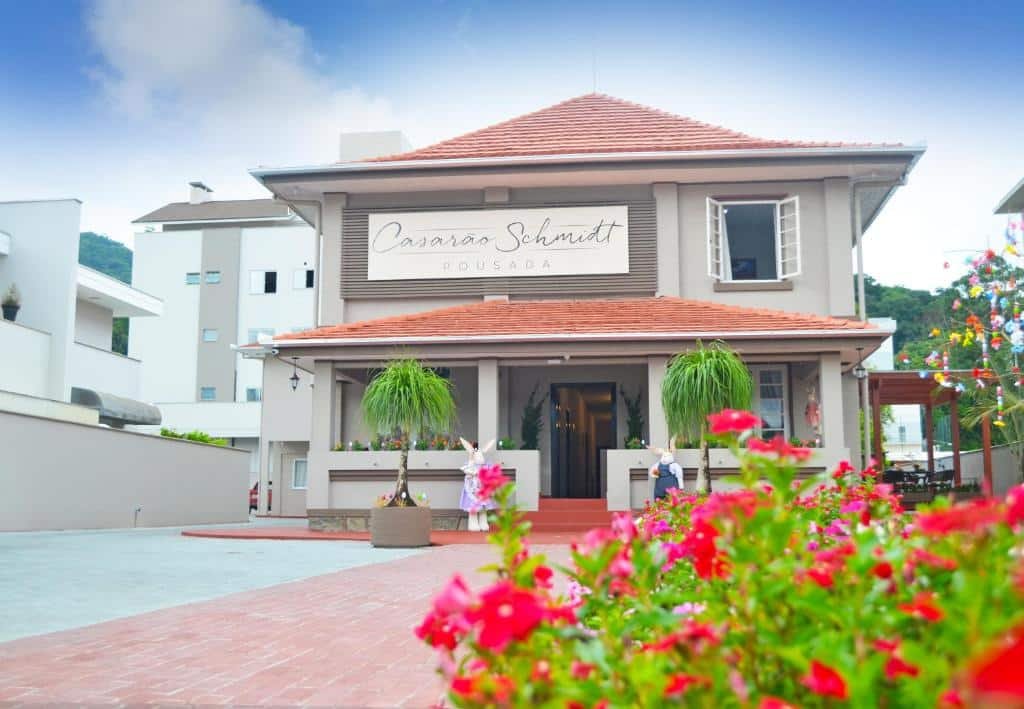 Frente da Pousada Casarão Schmidt. Um jardim, uma escada de três degraus e coelhos de decoração na frente..