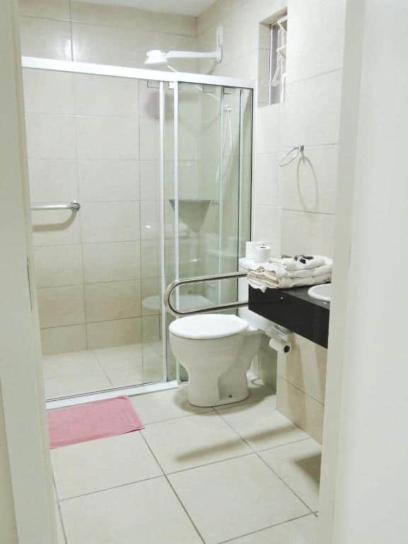 Banheiro com acessibilidade da Pousada Center. Um vaso sanitário com barra de apoio, atrás o box com uma barra de apoio.
