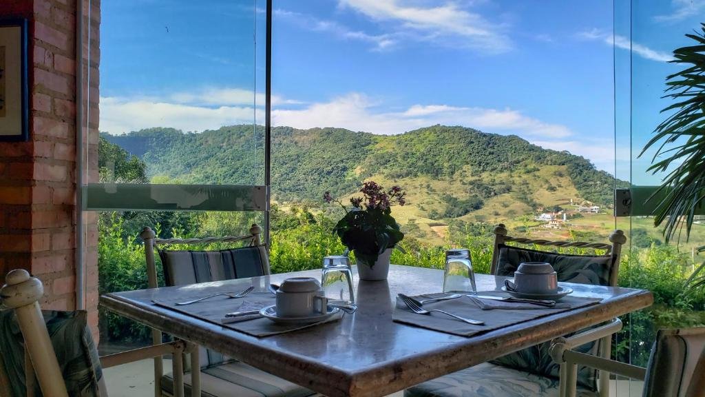 Vista da mesa de café da Pousada Vale do Dinossauro com quatro cadeiras feita de madeira e com vista linda das montanhas.