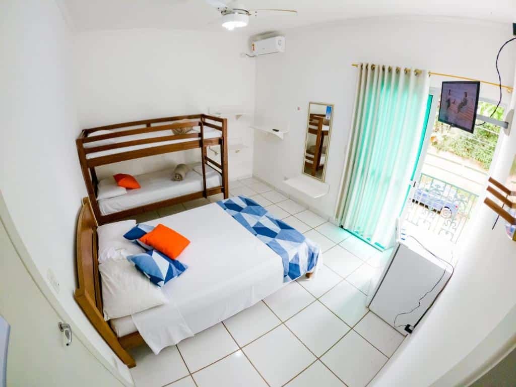 Quarto da Pousada entre as praias. Do lado esquerdo uma cama de casal e uma beliche. Do lado direito um frigobar, uma televisão, um espelho e a varanda. Foto para ilustrar post sobre pousadas pet friendly em Ubatuba.