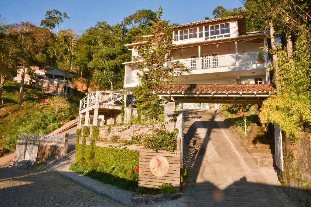 Fachada de dois andares da pousada in garden em Teresópolis com bastante árvores em volta e um morro para subir.