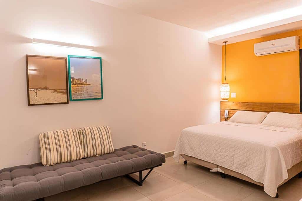 Quarto na Pousada Jamboo com uma cama de casal, um sofá com almofadas, dois quadros e um ar-condicionado