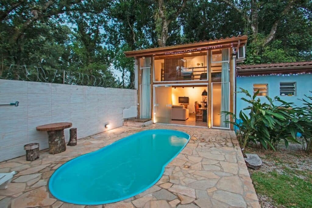 Piscina da Pousada Raio de Sol Maresias. Ela está em um espaço com chão de madeira e de frente para uma das acomodações.