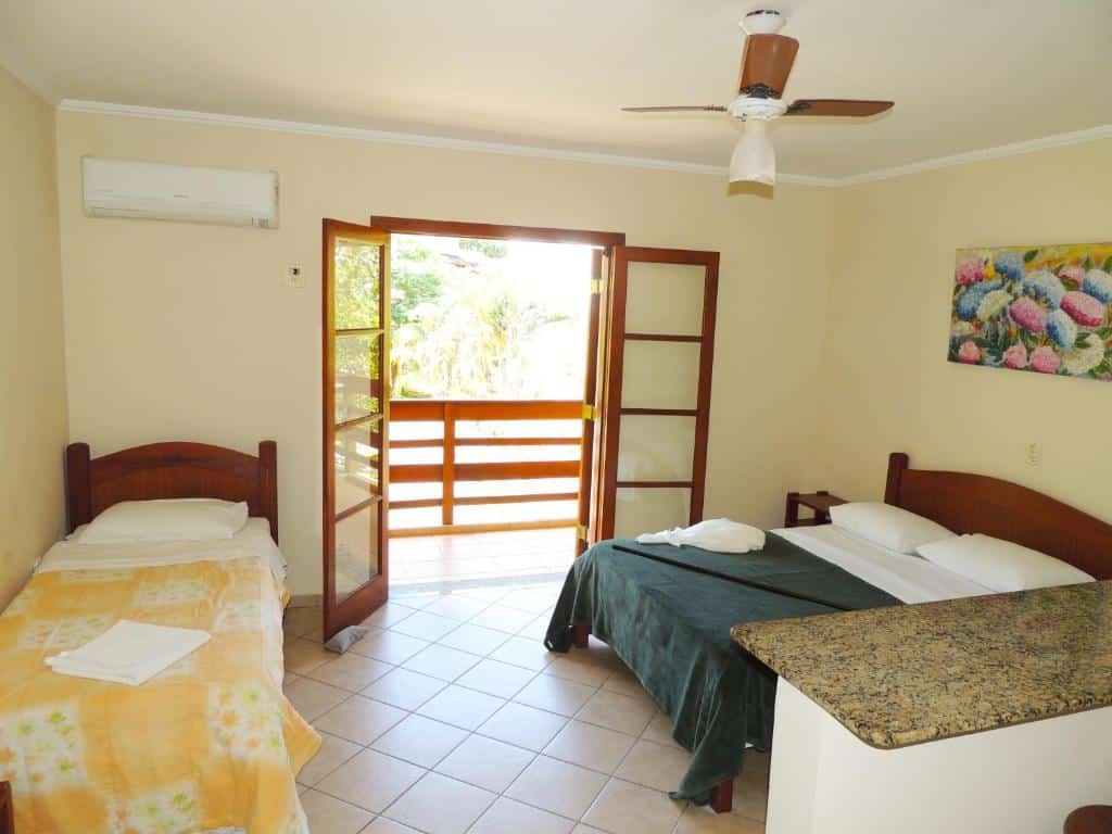 Quarto da Pousada Mosaico Brasil - Maresias com uma cama de casal e uma cama de solteiro em cada extremidade. No meio está a varanda.