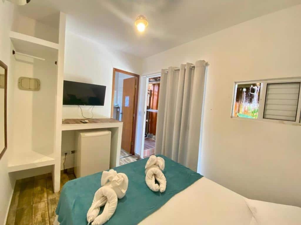 Quarto da Pousada Papaya Container. Uma cama de casal, de frente um frigobar, a televisão e a porta do banheiro. No fundo a janela e a porta do quarto. Foto para ilustrar post sobre pousadas pet friendly em Ubatuba.