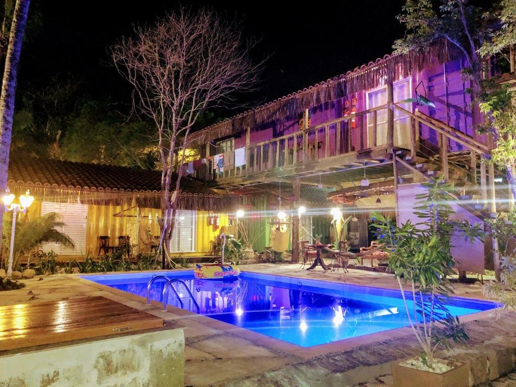 Área externa da Pousada Papaya Container. Uma piscina iluminada no meio, ao redor a pousada iluminada e árvores.