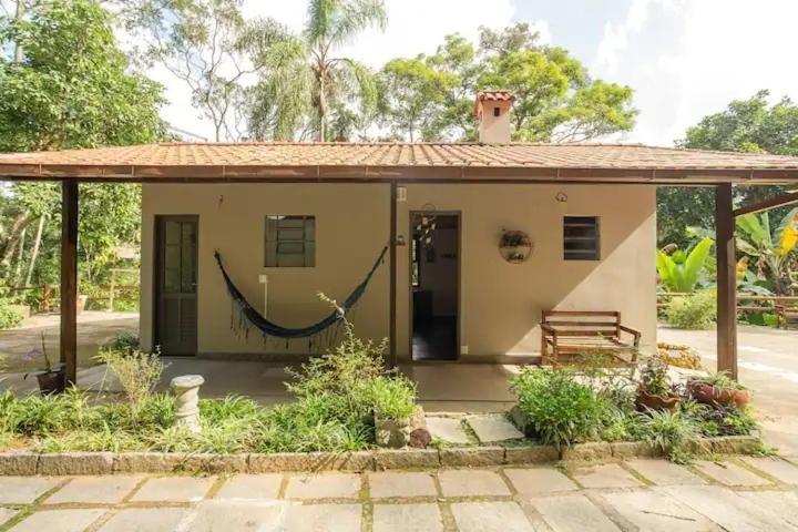 Fachada de uma das acomodações da pousada pé da tartaruga em Teresópolis com rede e banco de madeira e algumas árvores em volta.