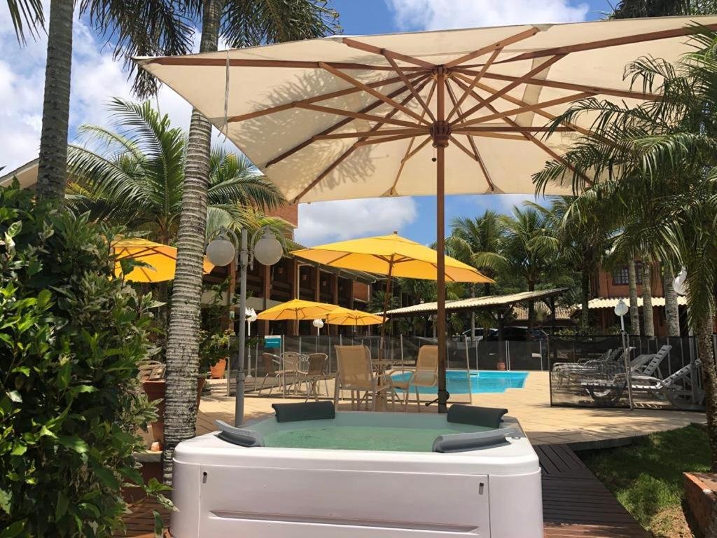 Área externa da Pousada Ponta do Lobo. Uma hidro com um guarda-sol, atrás a piscina com cadeiras de tomar sol e guarda-sóis.