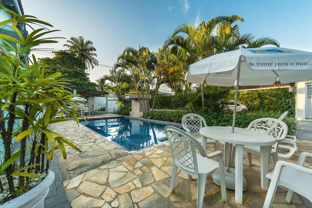 Área externa da Pousada Porto do Itagua. Uma piscina no centro, ao redor jardim, mesas e guarda-sóis.