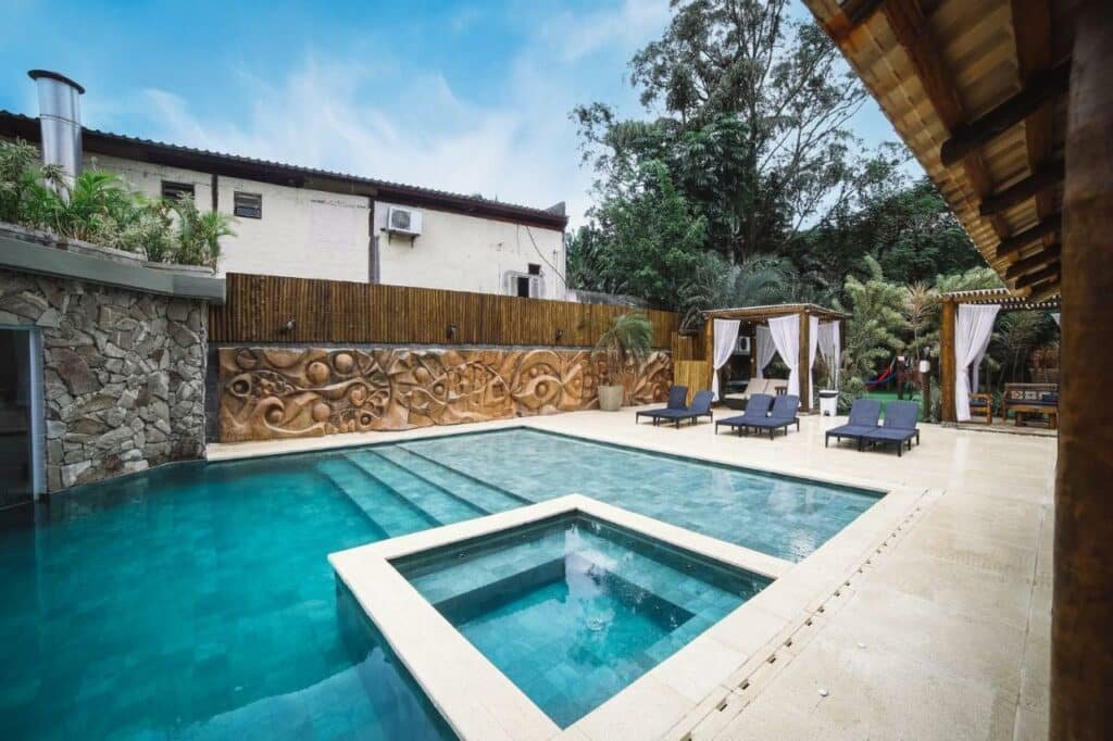 Piscina da Pousada Porto Mare. Ela é grande e possui uma parte separada e rasa. Ao redor estão espreguiçadeiras e áreas cobertas de descanso.
