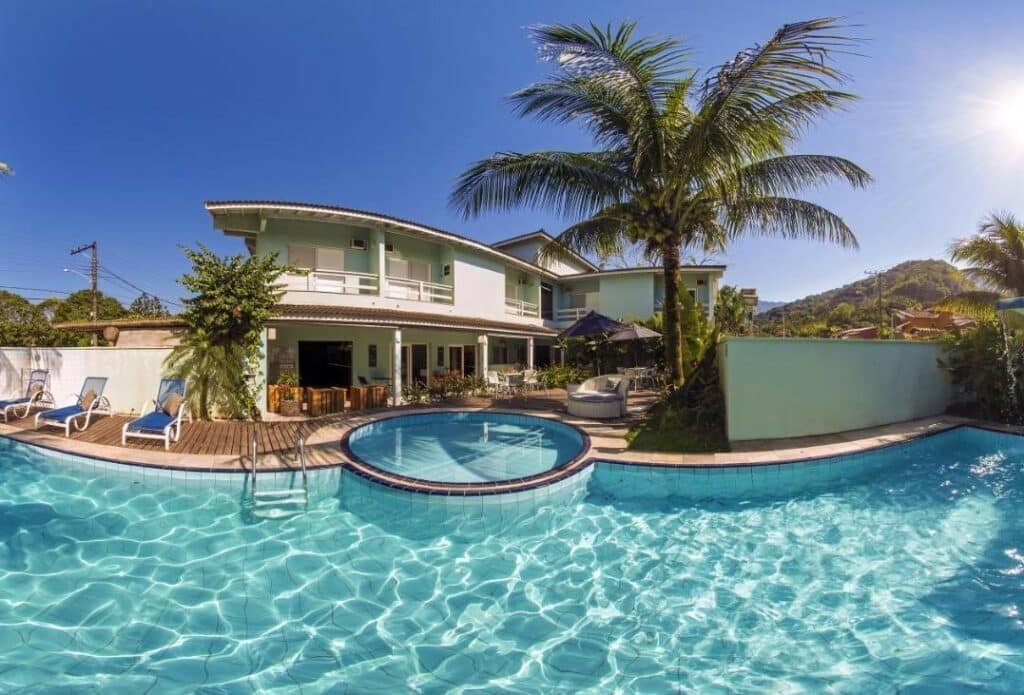 Piscina da Pousada Toca da Praia. Ela é bem grande e está de frente para a pousada. Perto dela estão algumas espreguiçadeiras.