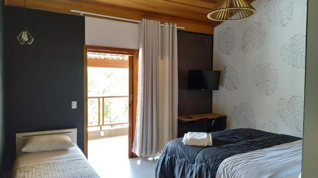 Quarto da Pousada Sítio Vale das Olivas com cama, TV e sacada.