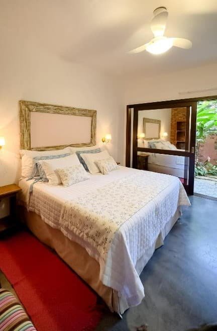 Quarto da Pousada Vila Rosada. Uma cama de casal, de cada lado uma mesinha de apoio e uma luminária. No fundo a porta da varanda. Foto para ilustrar post sobre pousadas pet friedly em Santa Catarina.